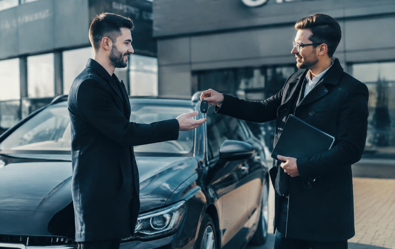 One person handing car keys to another beside a clean used car